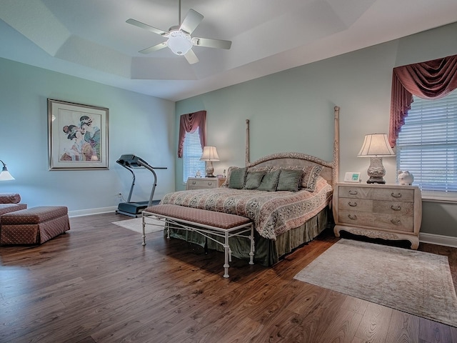 bedroom featuring dark wood-style floors, a ceiling fan, a raised ceiling, and baseboards