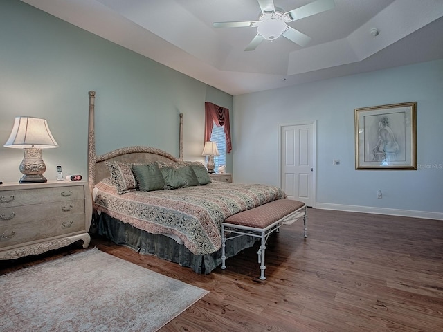 bedroom with ceiling fan, baseboards, a raised ceiling, and wood finished floors