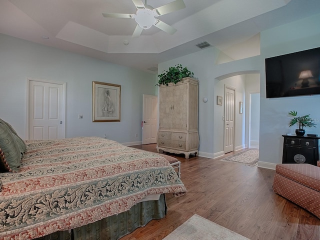 bedroom with visible vents, a tray ceiling, wood finished floors, arched walkways, and baseboards