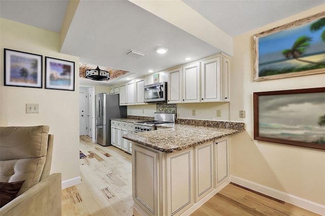 kitchen with stone countertops, stainless steel appliances, a peninsula, and light wood-style flooring