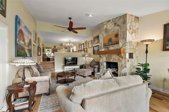 living room featuring visible vents, ceiling fan with notable chandelier, wood finished floors, a fireplace, and baseboards