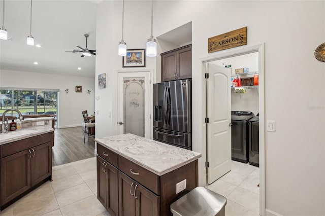 kitchen with dark brown cabinetry, pendant lighting, washer and dryer, stainless steel fridge, and a sink