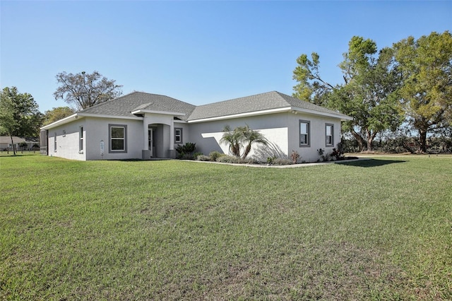 view of front facade featuring stucco siding, roof with shingles, and a front yard