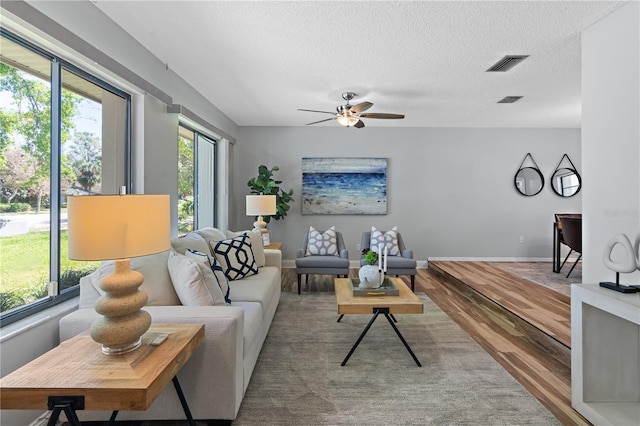 living room featuring visible vents, baseboards, wood finished floors, a textured ceiling, and a ceiling fan