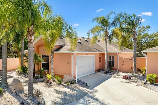 view of front of property featuring a shingled roof, fence, stucco siding, driveway, and an attached garage