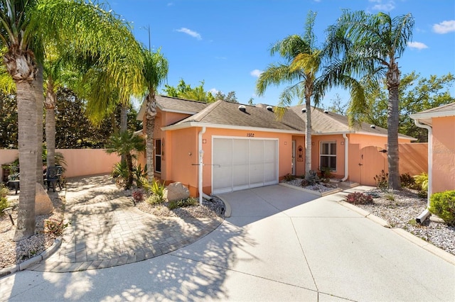 ranch-style house featuring a gate, fence, an attached garage, stucco siding, and concrete driveway