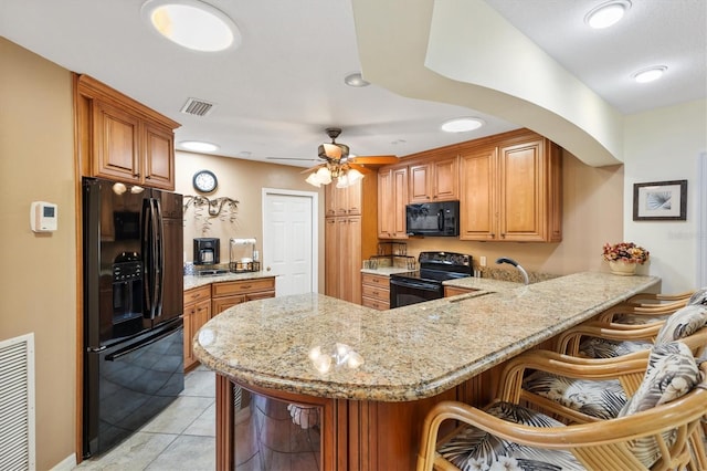 kitchen with visible vents, black appliances, a sink, a peninsula, and light stone countertops