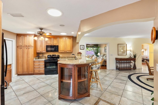 kitchen featuring light stone countertops, a peninsula, arched walkways, a sink, and black appliances