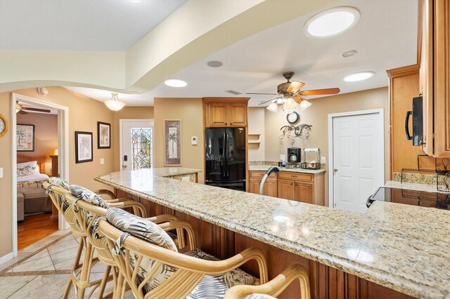 kitchen with a kitchen bar, black appliances, light stone counters, and a ceiling fan