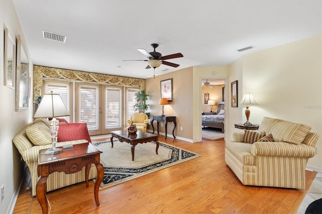 living area featuring a ceiling fan, light wood-style flooring, baseboards, and visible vents