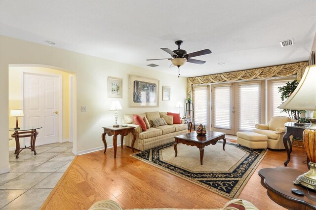 living room featuring light wood-type flooring, visible vents, baseboards, and a ceiling fan