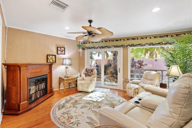 living room featuring light wood-type flooring, visible vents, a glass covered fireplace, recessed lighting, and a textured wall