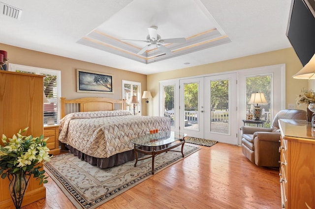 bedroom featuring a tray ceiling, visible vents, light wood finished floors, and access to outside