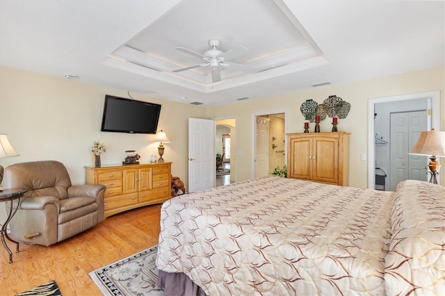 bedroom with a raised ceiling, light wood-style flooring, visible vents, and ornamental molding