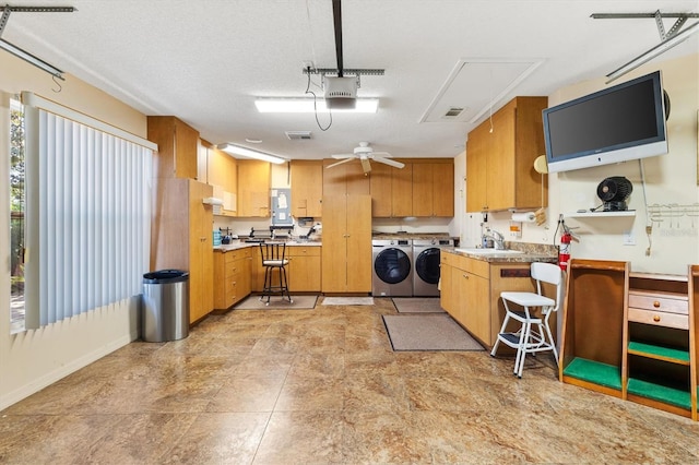 kitchen featuring brown cabinetry, a ceiling fan, a sink, light countertops, and washer and clothes dryer