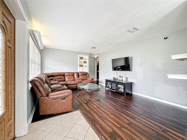 living area with baseboards, visible vents, light wood-type flooring, and a textured ceiling