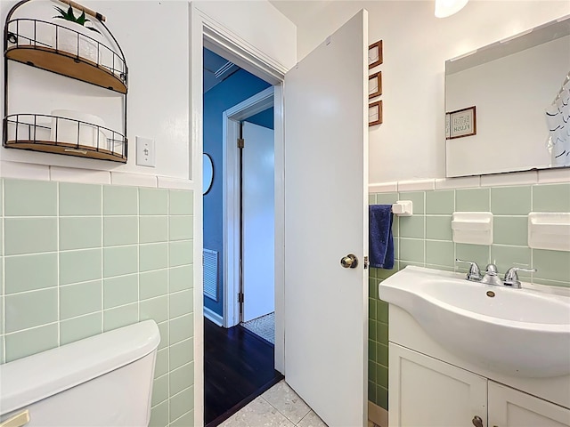 half bathroom with visible vents, toilet, tile walls, and vanity