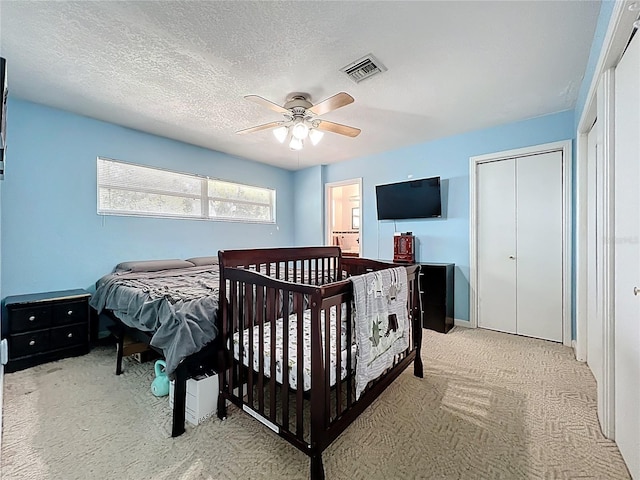 bedroom featuring visible vents, light colored carpet, a textured ceiling, and ceiling fan