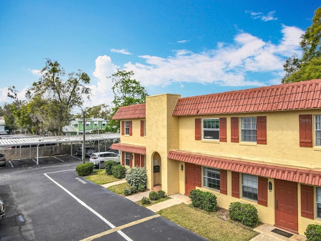 view of front of property with stucco siding, covered and uncovered parking, and a tiled roof