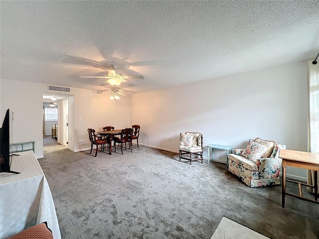 living area with a textured ceiling, carpet flooring, visible vents, and ceiling fan