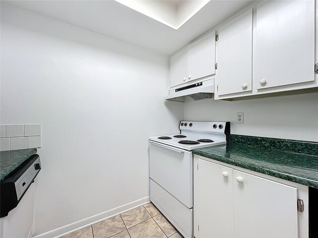 kitchen featuring white appliances, light tile patterned floors, white cabinets, under cabinet range hood, and dark countertops