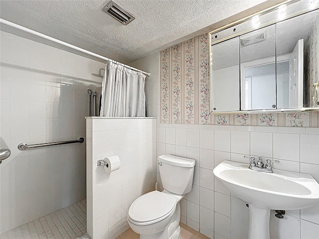 full bath with visible vents, tile walls, toilet, a tile shower, and a textured ceiling