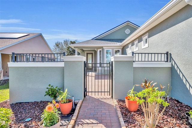 view of exterior entry featuring stucco siding, a gate, fence, a shingled roof, and a balcony