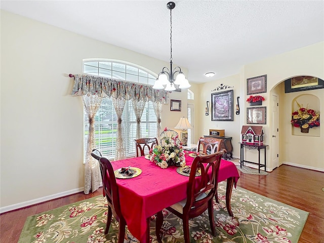 dining room with a notable chandelier, wood finished floors, baseboards, and a textured ceiling