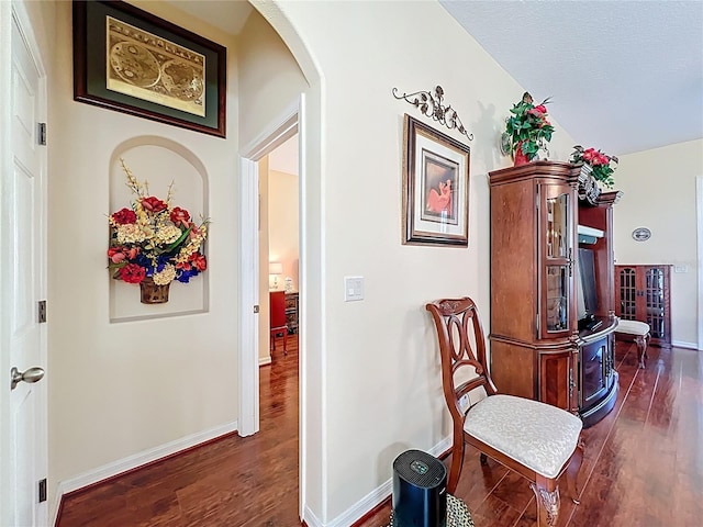 hallway with dark wood-style floors, baseboards, and arched walkways