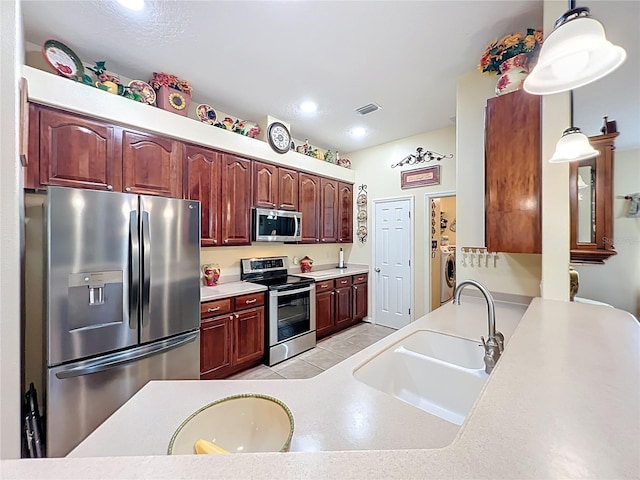 kitchen featuring washing machine and clothes dryer, visible vents, decorative light fixtures, stainless steel appliances, and a sink