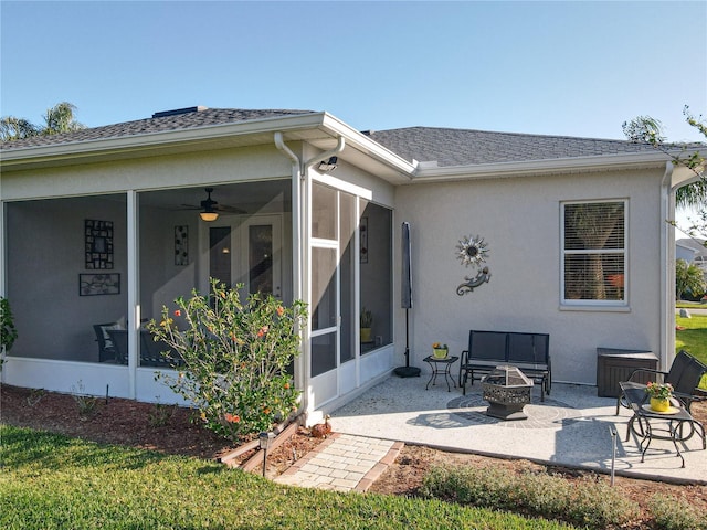 rear view of house with stucco siding, a patio, a fire pit, roof with shingles, and a sunroom