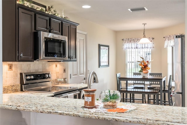 kitchen with light stone countertops, hanging light fixtures, dark brown cabinetry, appliances with stainless steel finishes, and backsplash