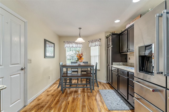 kitchen with tasteful backsplash, baseboards, stainless steel fridge with ice dispenser, light wood-type flooring, and hanging light fixtures