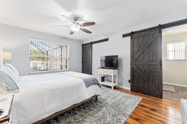 bedroom with a ceiling fan, a barn door, wood finished floors, and baseboards