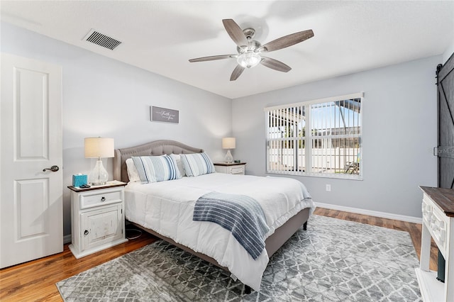 bedroom featuring ceiling fan, visible vents, baseboards, and wood finished floors