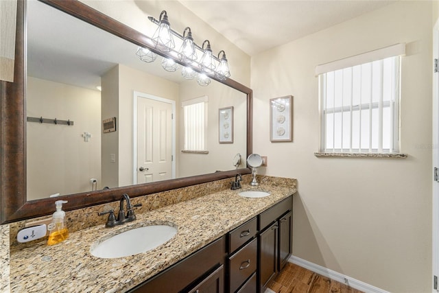 bathroom with a sink, baseboards, wood finished floors, and double vanity