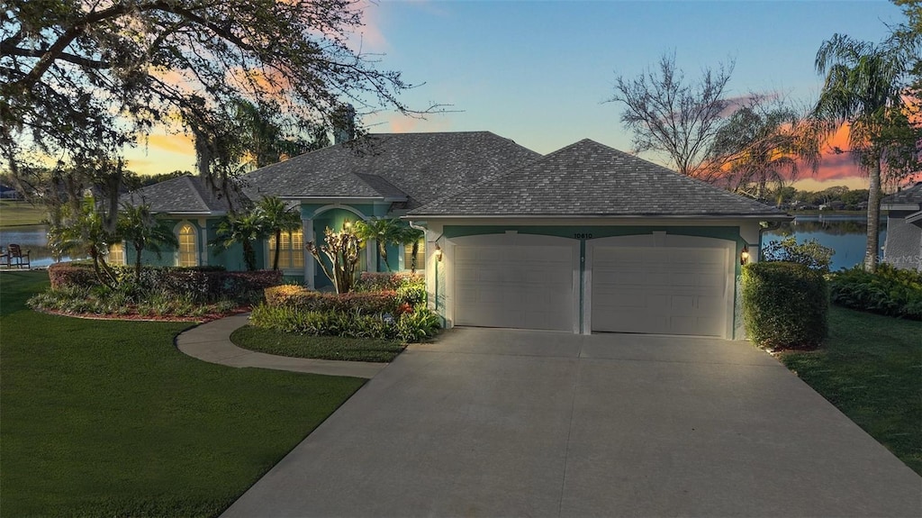 view of front of property with a water view, an attached garage, concrete driveway, and a front lawn