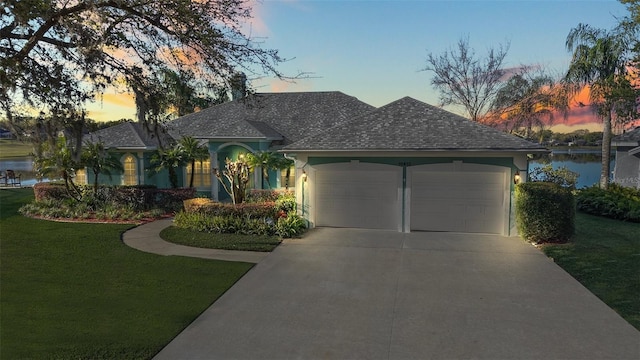 view of front of property with a water view, an attached garage, concrete driveway, and a front lawn