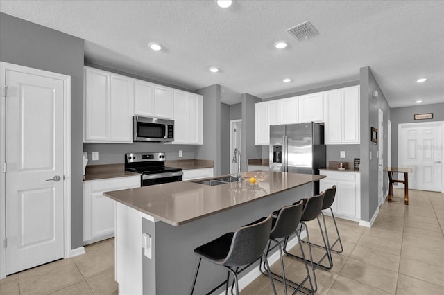 kitchen with an island with sink, a kitchen bar, light tile patterned floors, appliances with stainless steel finishes, and a sink