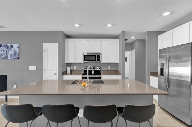 kitchen with a breakfast bar, recessed lighting, a sink, stainless steel appliances, and white cabinetry