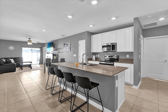 kitchen with a sink, open floor plan, appliances with stainless steel finishes, a breakfast bar area, and light tile patterned floors