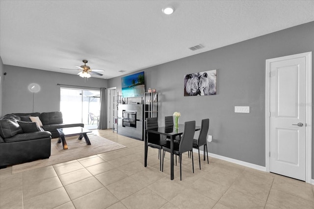 dining room featuring visible vents, a glass covered fireplace, light tile patterned floors, baseboards, and ceiling fan