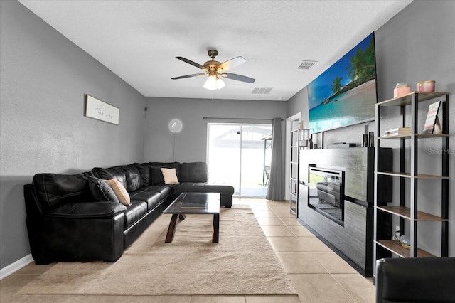 living room with a glass covered fireplace, tile patterned floors, a ceiling fan, and visible vents