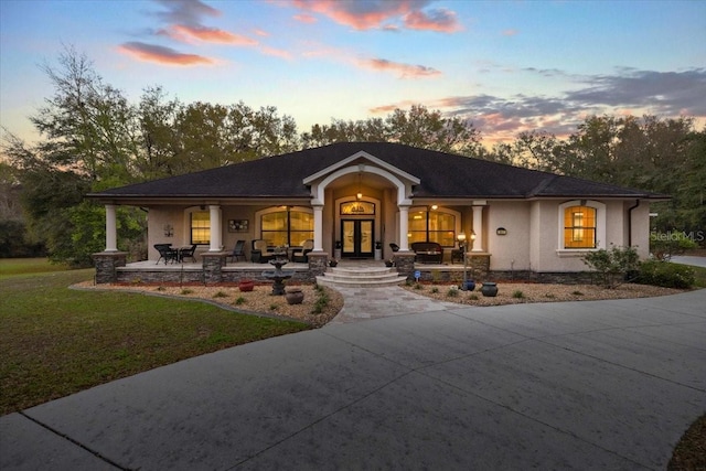 view of front facade with a front yard, french doors, covered porch, and stucco siding