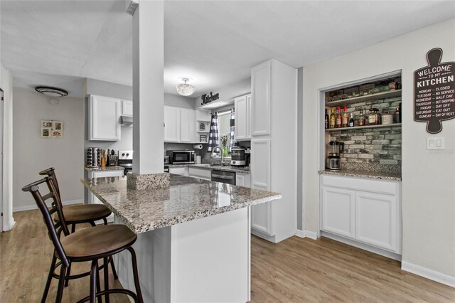 3058 SE 3rd Ave, Ocala, FL 34471 - kitchen featuring light stone counters, light wood finished floors, white cabinetry, appliances with stainless steel finishes, and a kitchen bar