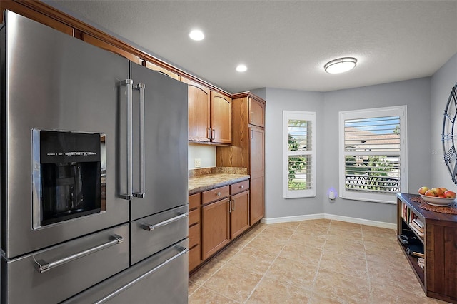 kitchen featuring baseboards, light countertops, recessed lighting, brown cabinetry, and high end fridge