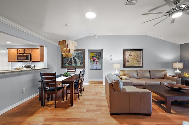 living area with vaulted ceiling, visible vents, light wood finished floors, and ornamental molding