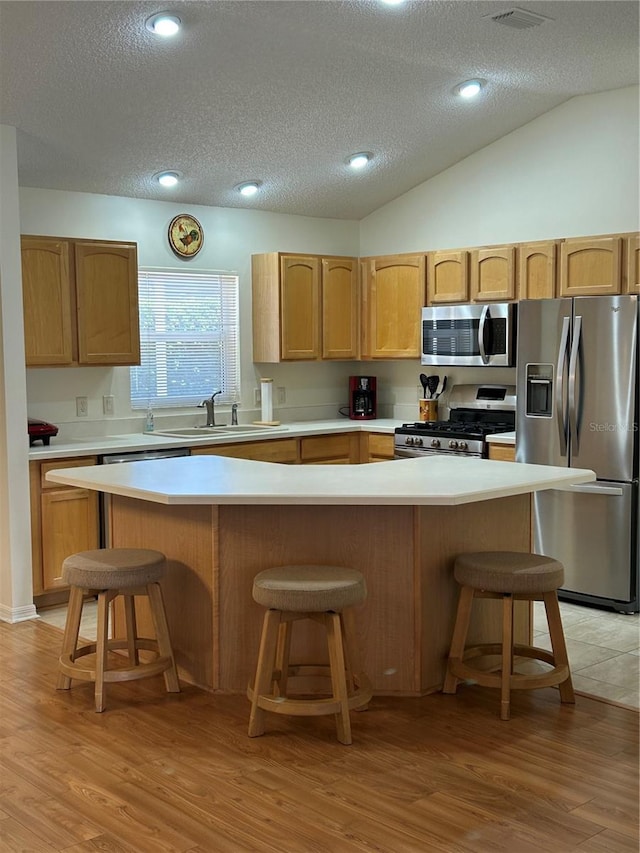 kitchen featuring light wood finished floors, a breakfast bar, light countertops, appliances with stainless steel finishes, and a sink