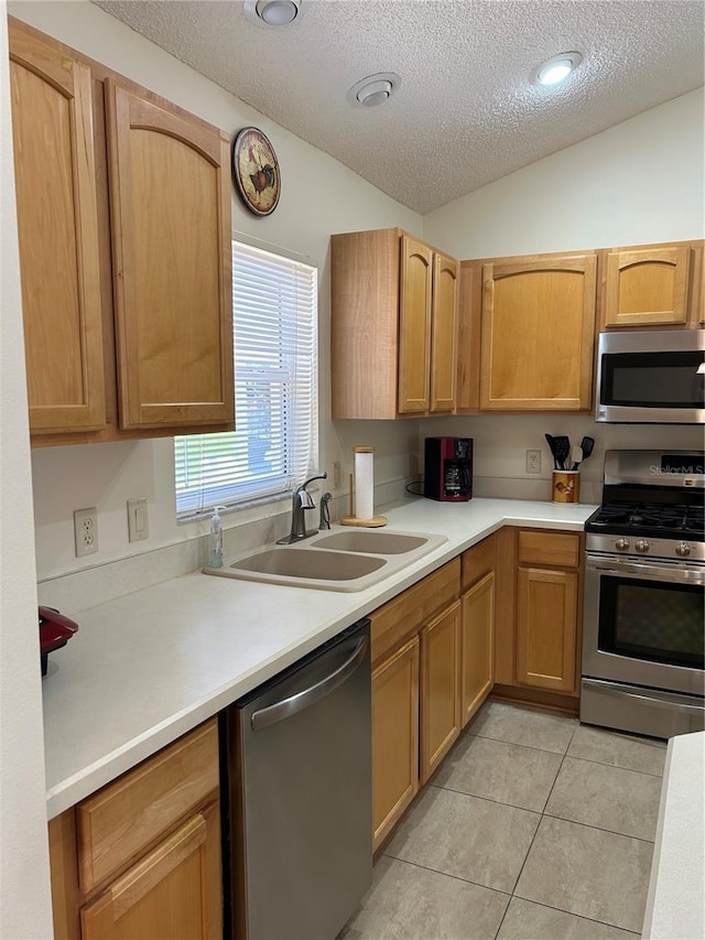 kitchen featuring light countertops, vaulted ceiling, light tile patterned flooring, stainless steel appliances, and a sink