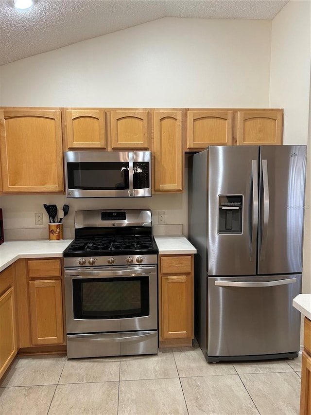 kitchen with light countertops, vaulted ceiling, appliances with stainless steel finishes, light tile patterned flooring, and a textured ceiling